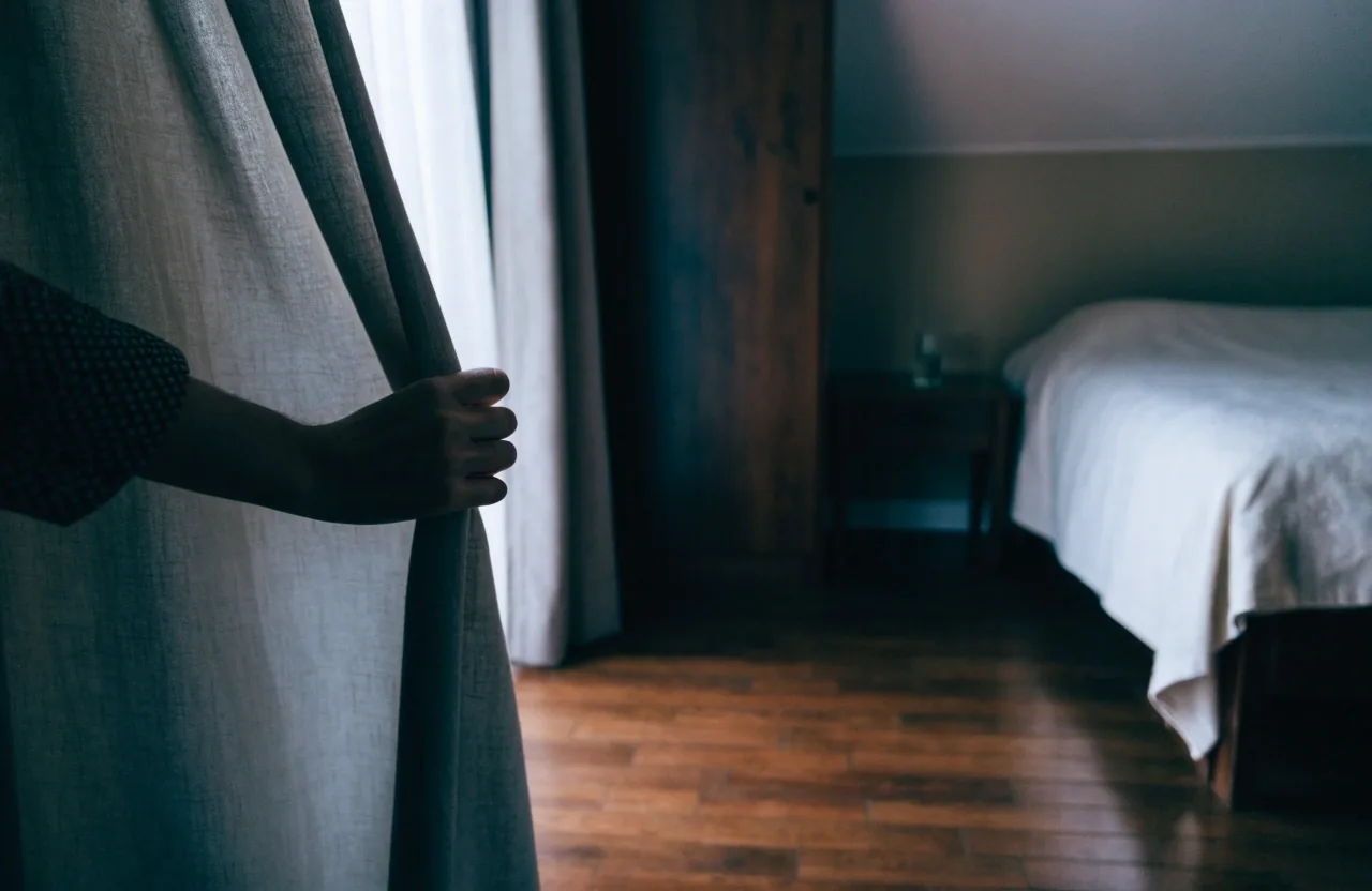 A quiet bedroom at dawn with a made bed, water glass and a watch set aside on the nightstand