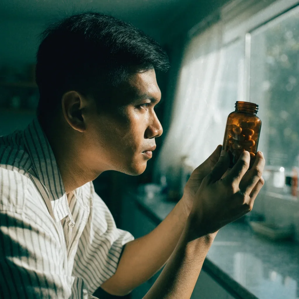 Hands holding a plain bottle up to window light while inspecting it at a kitchen counter